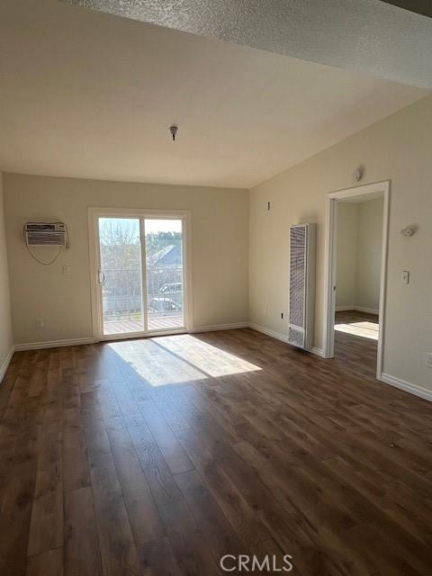 empty room featuring dark wood-style floors, a wall unit AC, lofted ceiling, and baseboards