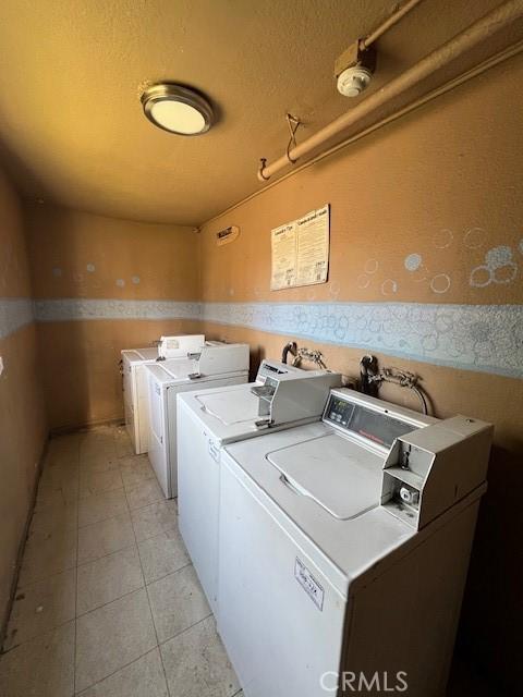 community laundry room with washer and clothes dryer, a textured ceiling, and light tile patterned floors