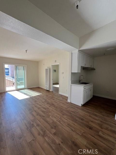 unfurnished living room featuring dark wood-type flooring, a sink, and baseboards