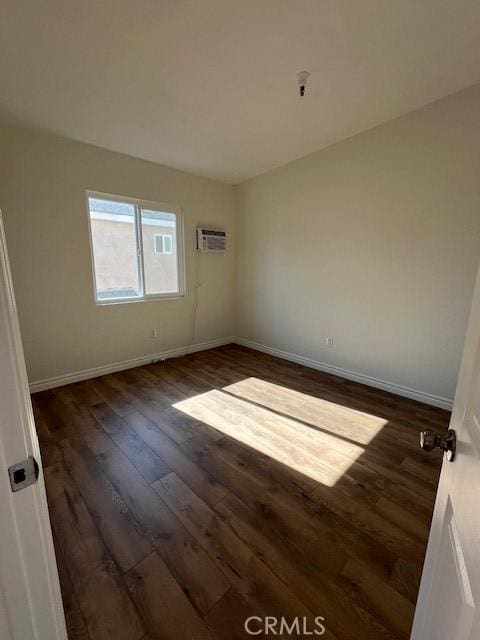 empty room with dark wood-style flooring, an AC wall unit, and baseboards