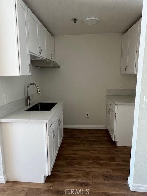 kitchen featuring baseboards, dark wood finished floors, light countertops, white cabinetry, and a sink