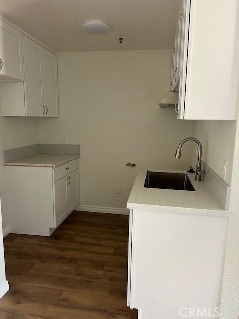 kitchen with dark wood finished floors, white cabinets, light countertops, and a sink