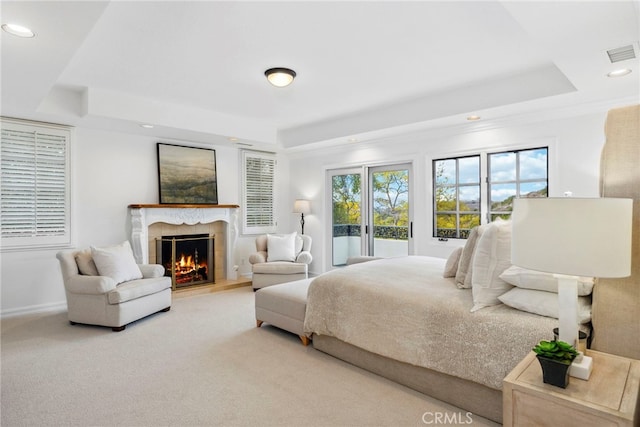 bedroom featuring light carpet, a fireplace, and a tray ceiling