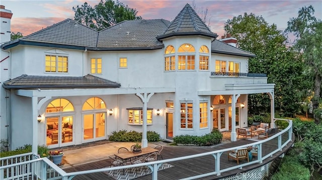 back house at dusk featuring a wooden deck, a balcony, and an outdoor hangout area