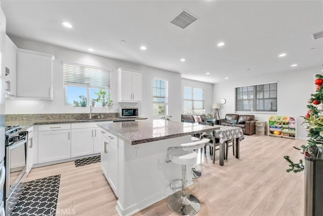 kitchen with visible vents, open floor plan, white cabinets, a sink, and dark stone countertops