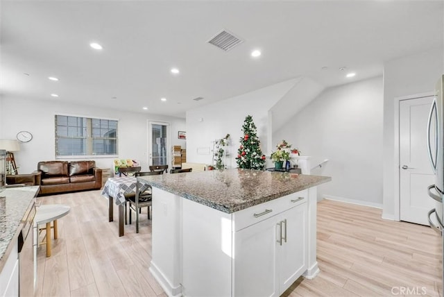 kitchen with a kitchen island, visible vents, white cabinetry, open floor plan, and light stone countertops