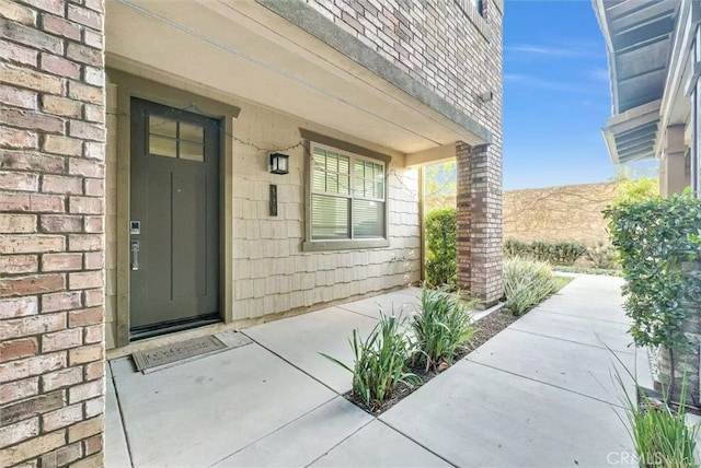 entrance to property featuring a shingled roof and brick siding