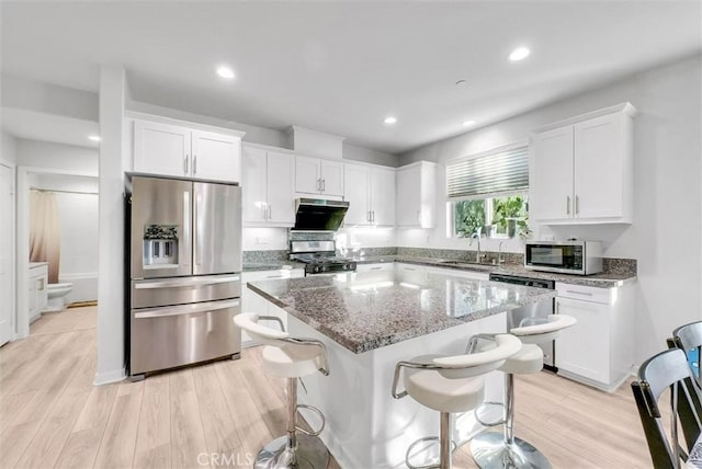 kitchen with a breakfast bar, a sink, a kitchen island, white cabinetry, and appliances with stainless steel finishes