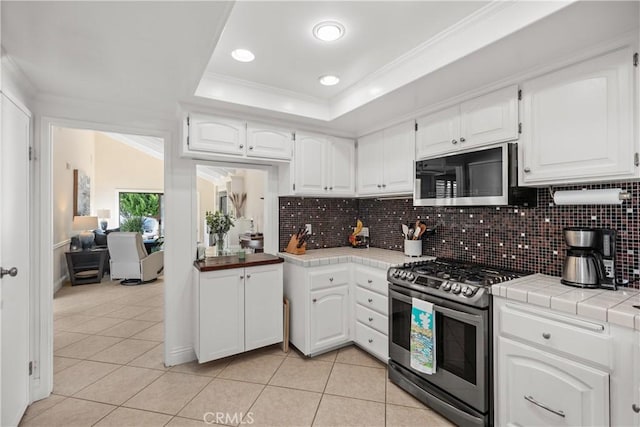 kitchen featuring a tray ceiling, tile countertops, white cabinets, and appliances with stainless steel finishes