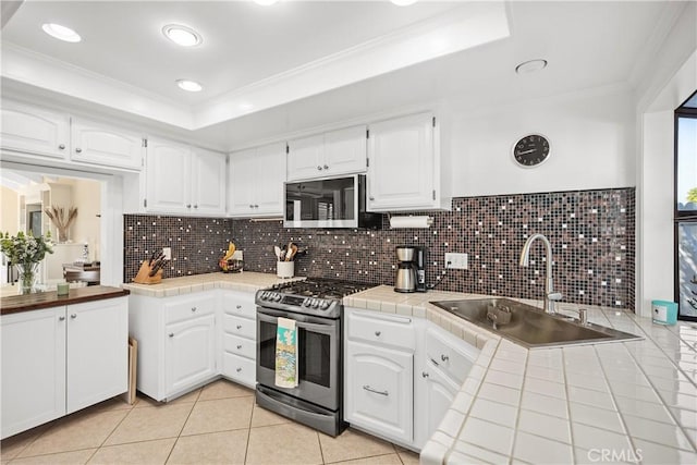 kitchen featuring appliances with stainless steel finishes, tile countertops, white cabinets, and a tray ceiling