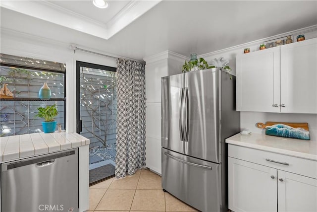 kitchen featuring light tile patterned flooring, tile countertops, white cabinetry, ornamental molding, and stainless steel appliances