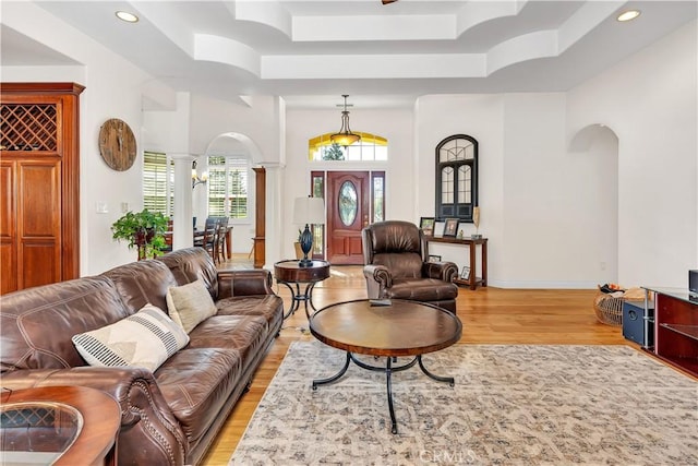 living room featuring a tray ceiling, decorative columns, and light wood-type flooring