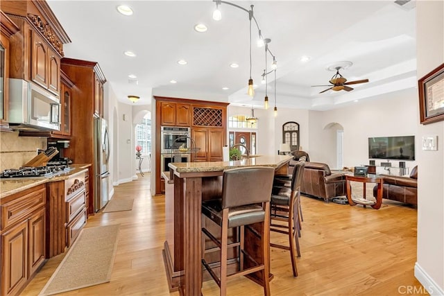 kitchen featuring a kitchen bar, a center island with sink, pendant lighting, stainless steel appliances, and backsplash