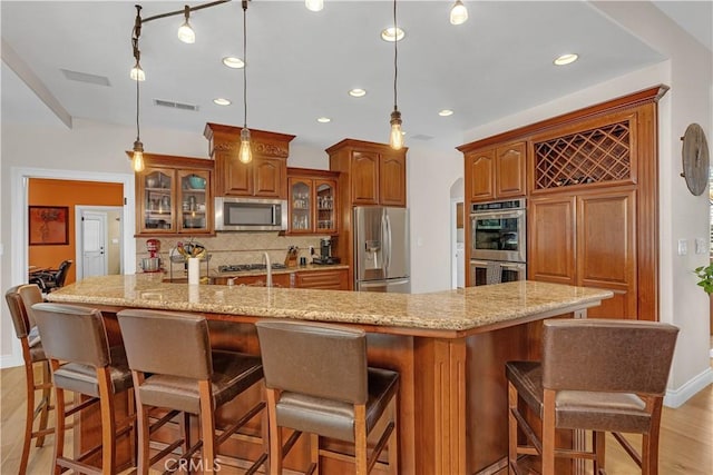 kitchen with stainless steel appliances, tasteful backsplash, a kitchen bar, and a large island with sink