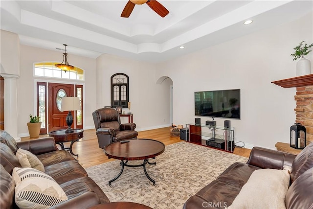 living room with ceiling fan, a tray ceiling, decorative columns, and light hardwood / wood-style flooring