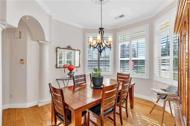 dining area featuring ornate columns, ornamental molding, an inviting chandelier, and light hardwood / wood-style flooring