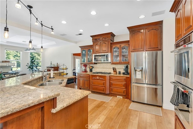 kitchen with pendant lighting, sink, light hardwood / wood-style floors, stainless steel appliances, and light stone countertops