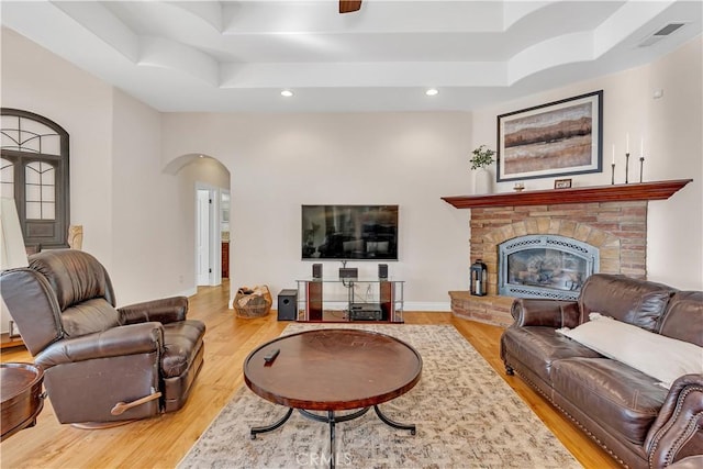 living room featuring hardwood / wood-style flooring, a tray ceiling, and a stone fireplace