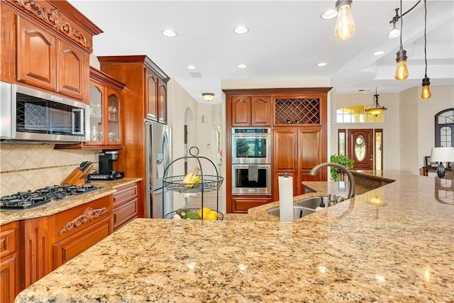 kitchen with pendant lighting, appliances with stainless steel finishes, light stone countertops, and sink