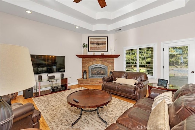 living room featuring ceiling fan, a fireplace, a raised ceiling, and light hardwood / wood-style floors