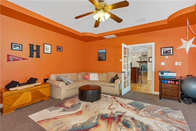 carpeted living room with a raised ceiling, ceiling fan, and french doors