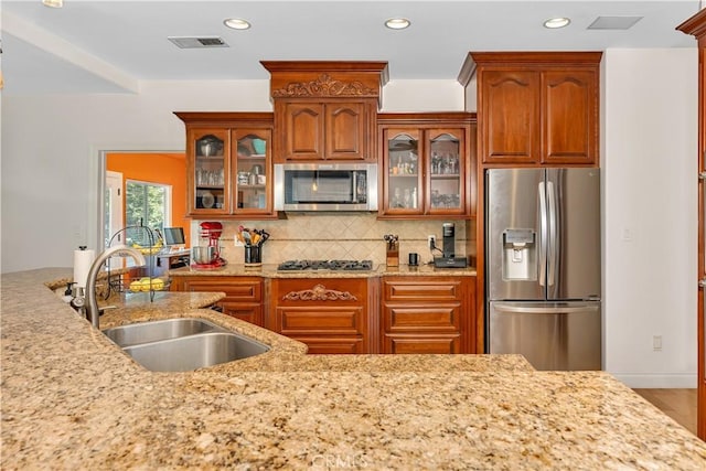 kitchen with appliances with stainless steel finishes, hardwood / wood-style floors, tasteful backsplash, sink, and light stone countertops