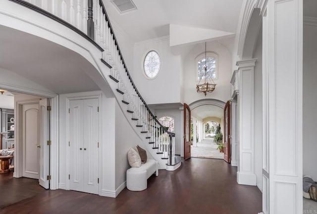 entryway featuring ornate columns, a towering ceiling, dark hardwood / wood-style flooring, a notable chandelier, and crown molding