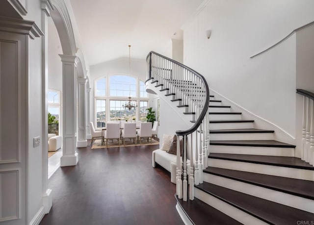 stairway featuring a notable chandelier, high vaulted ceiling, hardwood / wood-style floors, and ornate columns