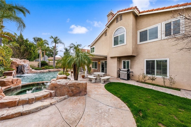 back of property with pool water feature, an in ground hot tub, and a patio