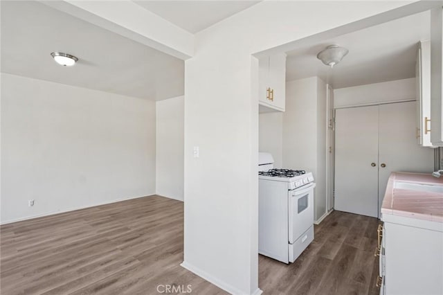 kitchen with white range with gas stovetop, white cabinets, wood finished floors, a sink, and tile counters