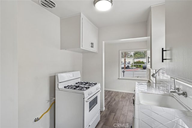 kitchen featuring dark wood finished floors, white cabinets, visible vents, gas range gas stove, and a sink