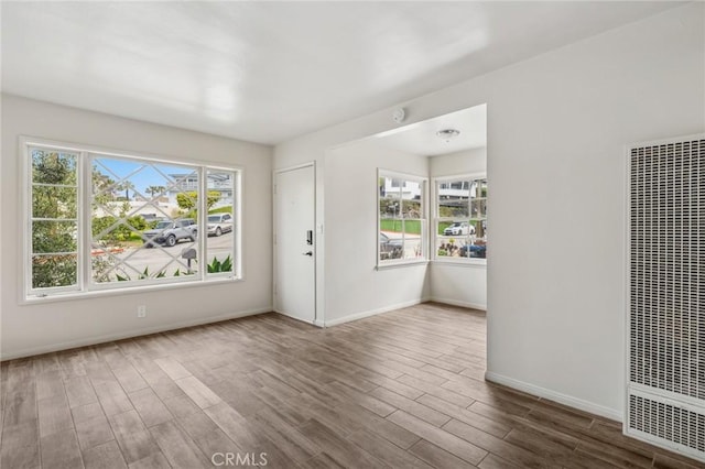 empty room with plenty of natural light, a heating unit, baseboards, and wood finished floors