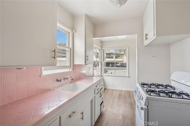 kitchen with light wood-style flooring, white gas range, white cabinets, tile countertops, and a sink