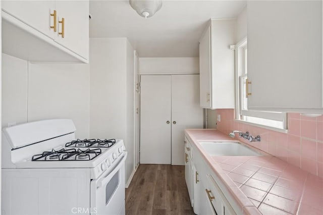 kitchen featuring white gas range oven, white cabinetry, dark wood finished floors, tile countertops, and a sink