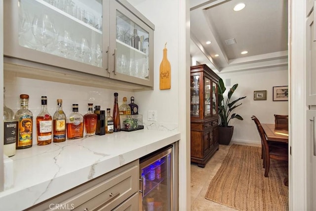 bar featuring wine cooler, a tray ceiling, and light stone countertops