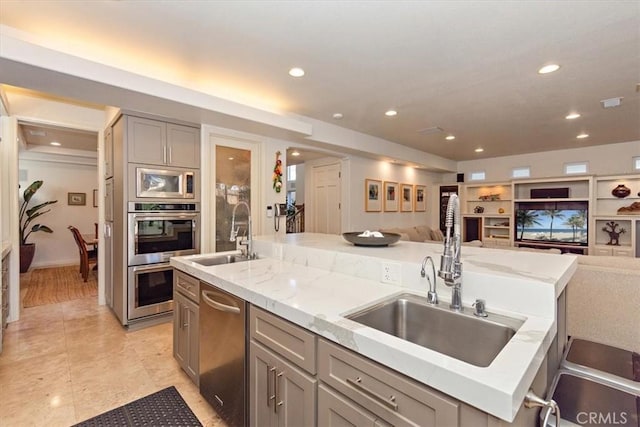 kitchen featuring sink, gray cabinets, stainless steel appliances, and an island with sink