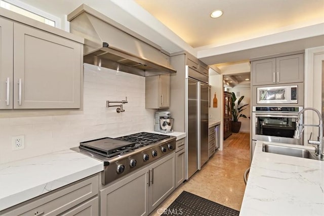 kitchen with sink, built in appliances, gray cabinets, custom range hood, and backsplash