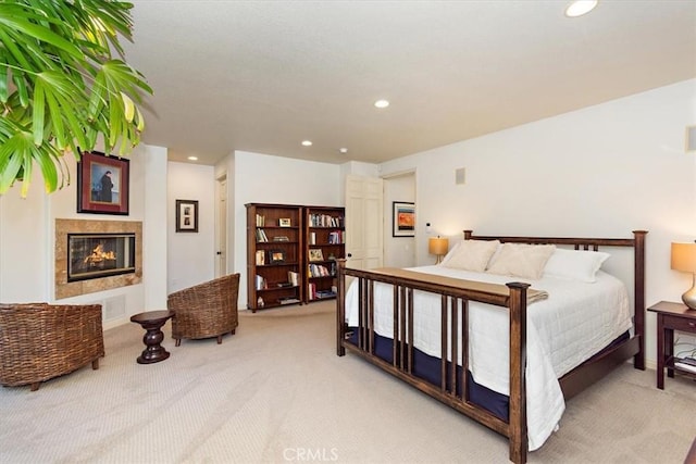 bedroom with a tiled fireplace and light carpet