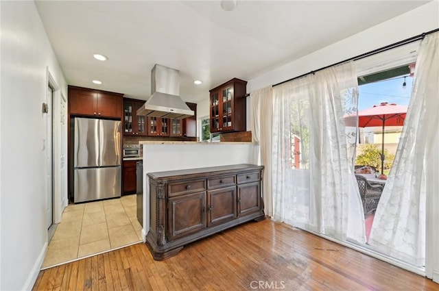 kitchen with a toaster, island exhaust hood, glass insert cabinets, freestanding refrigerator, and light wood-style floors