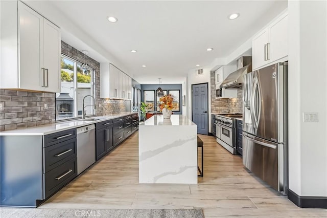 kitchen with wall chimney range hood, stainless steel appliances, white cabinets, and a kitchen island