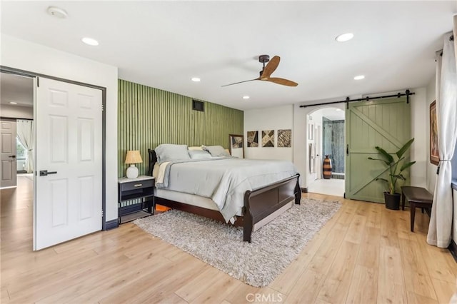 bedroom with ceiling fan, a barn door, and light wood-type flooring