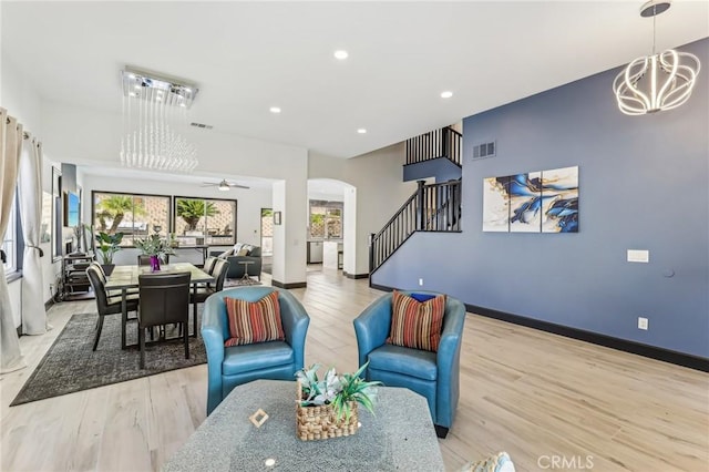 living room with ceiling fan with notable chandelier and light hardwood / wood-style flooring