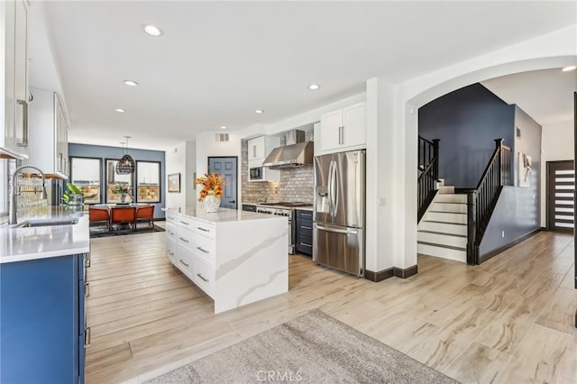 kitchen with sink, appliances with stainless steel finishes, white cabinets, a kitchen island, and wall chimney exhaust hood