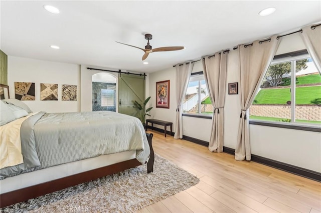 bedroom with ceiling fan, a barn door, and light wood-type flooring