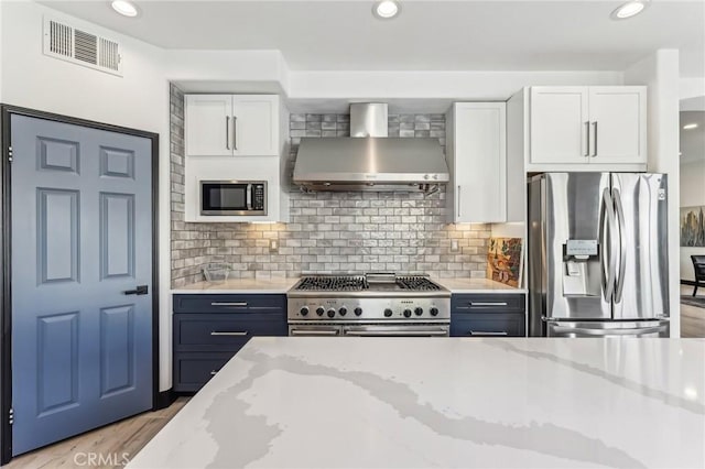 kitchen with light stone counters, wall chimney range hood, white cabinets, and appliances with stainless steel finishes