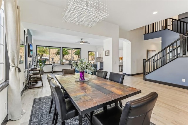 dining space with ceiling fan with notable chandelier and light hardwood / wood-style flooring