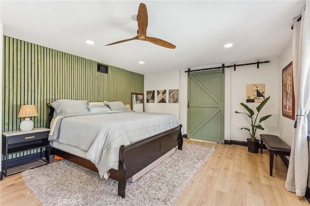 bedroom with a barn door, ceiling fan, and light wood-type flooring