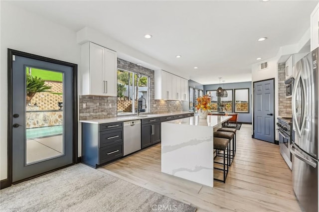 kitchen featuring a breakfast bar, white cabinetry, stainless steel appliances, a center island, and decorative light fixtures