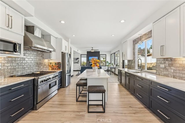 kitchen featuring white cabinetry, wall chimney range hood, stainless steel appliances, and a kitchen island