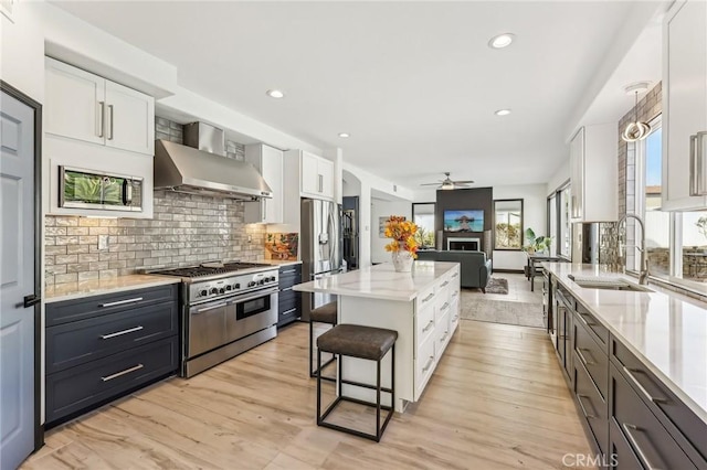 kitchen featuring appliances with stainless steel finishes, decorative light fixtures, white cabinetry, sink, and wall chimney range hood